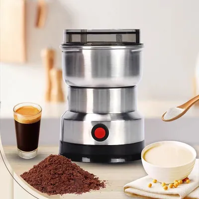 Moedor elétrico cilíndrico de inox com tampa transparente e botão vermelho, ao lado de café moído, café no copo e grãos
