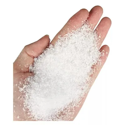 Mão aberta segurando um punhado de neve artificial branca em flocos finos, sobre fundo branco