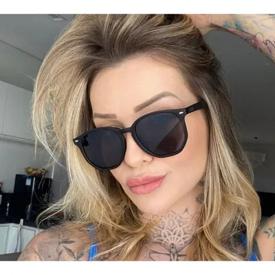 Mulher loira usando óculos de sol de armação preta fosca arredondada, lentes escuras e pequenos rebites prateados