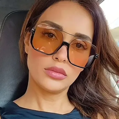 Mulher de cabelo castanho no carro usando óculos quadrados grandes de lente âmbar clara, aro preto embaixo e ponte dupla