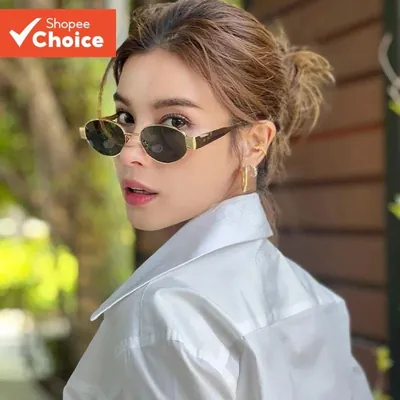 Mulher de camisa branca usando óculos de sol oval com armação dourada e lentes escuras