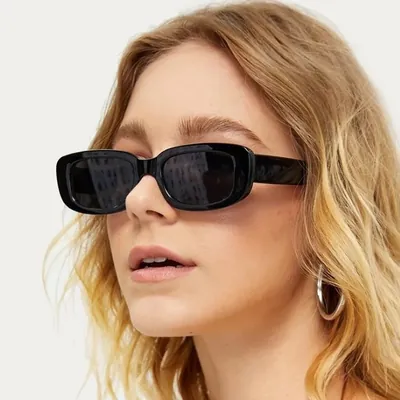 Mulher loira de brinco de argola usando óculos de sol retangular estreito com armação preta e lentes escuras