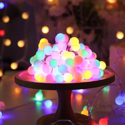 Cordão de luzes de bolinhas foscas acesas em rosa, azul, verde e amarelo, empilhado sobre suporte de madeira