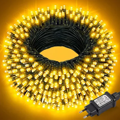 Cordão de LED enrolado com centenas de luzes amareladas acesas, fio verde-escuro e fonte preta com plugue de pinos redondos