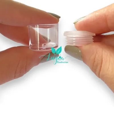 Dedos segurando um potinho de plástico transparente e sua tampa de rosca translúcida, separados