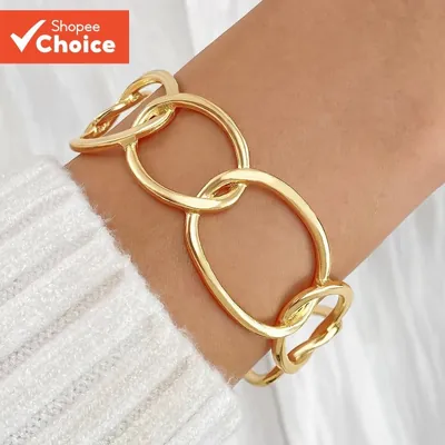 Bracelete dourado aberto formado por elos ovais grandes e irregulares no pulso de mulher com suéter branco