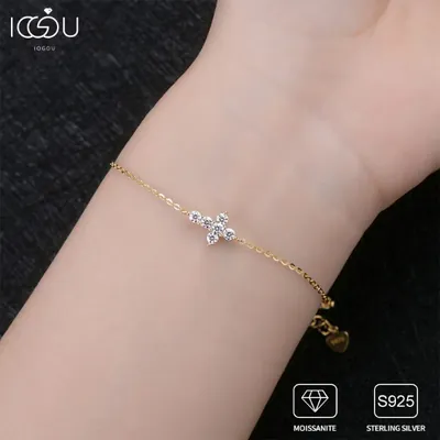 Pulseira dourada de corrente fina com cruz de pedrinhas redondas no pulso, com extensor e plaquinha de coração