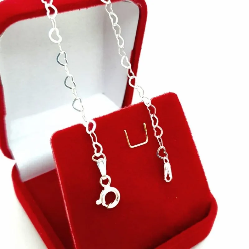 Pulseira prateada de elos em coração vazado com fecho de argola, apoiada em caixa de veludo vermelho
