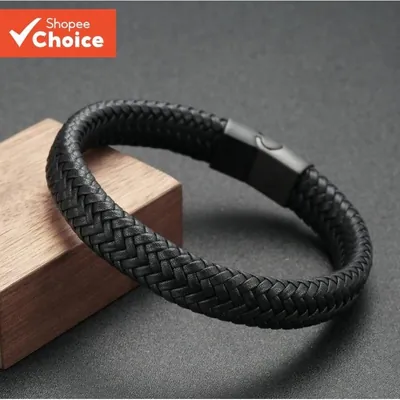 Pulseira de couro preto trançado em espinha de peixe com fecho retangular preto fosco, apoiada num bloco de madeira