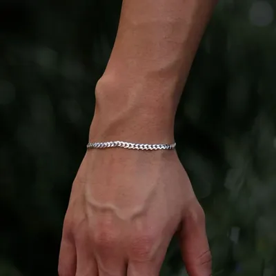 Pulso masculino com pulseira grumet prateada fina sobre fundo de folhagem verde desfocada