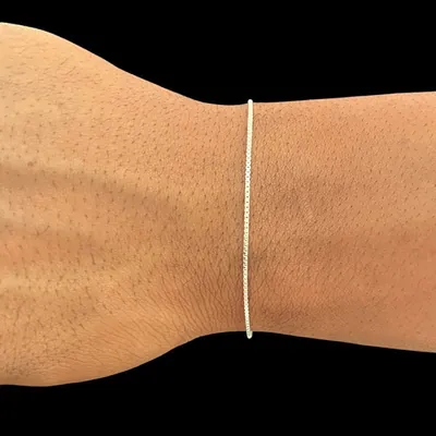Pulso masculino com pulseira prateada muito fina de malha veneziana, sobre fundo preto