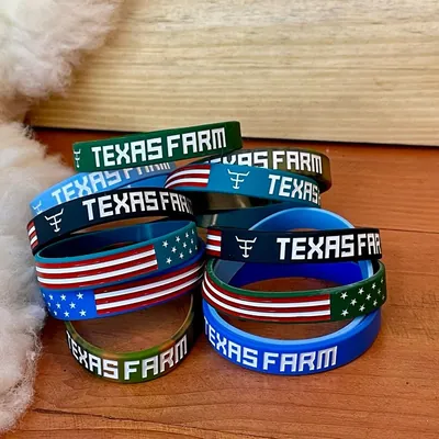 Várias pulseiras de silicone Texas Farm em verde, azul e preto, algumas com bandeira dos EUA, sobre madeira