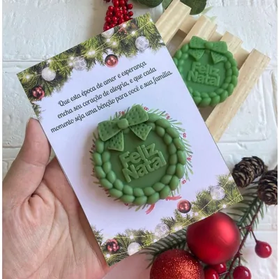 Sabonete verde em forma de guirlanda com laço e Feliz Natal, preso a cartão ilustrado com mensagem de fim de ano