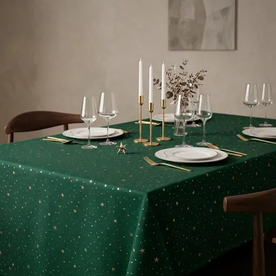 Mesa com toalha verde-escura de estrelinhas douradas, pratos brancos, talheres dourados e castiçais com velas brancas