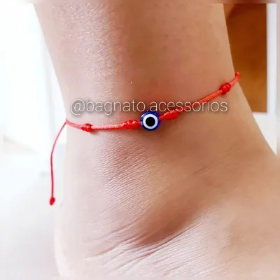 Tornozelo com tornozeleira de cordão vermelho fino, pequenos nós e uma conta redonda de olho grego azul no meio