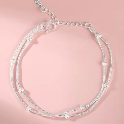 Tornozeleira prateada de duas correntes finas com bolinhas espaçadas, fecho e extensor, sobre fundo rosa