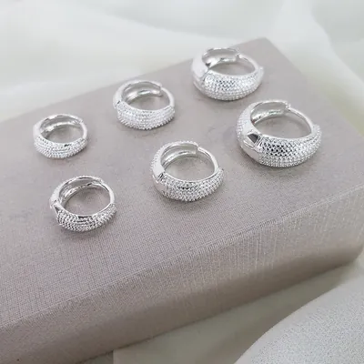 Três pares de argolinhas prateadas em formato gota com textura de bolinhas, em tamanhos crescentes, sobre caixa bege