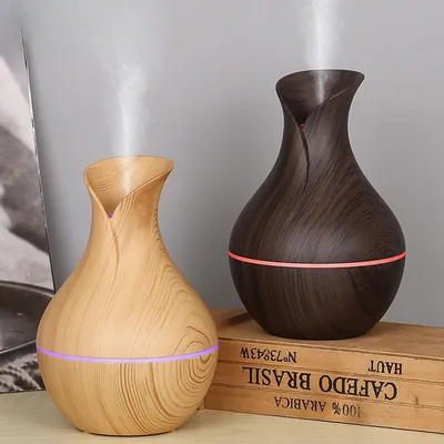 Dois umidificadores em formato de vaso, um madeira clara e outro escuro, soltando névoa e com faixa de luz LED