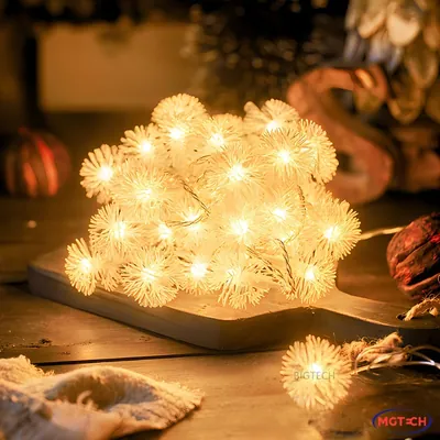 Varal de luzes com bolinhas brancas felpudas acesas em luz amarela, amontoado sobre tábua de madeira