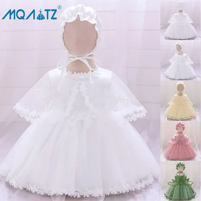 Vestido branco de bebê em manequim, com saia de tule, barra de renda, capinha transparente e touca amarrada com fita