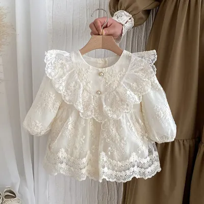 Vestido de bebê marfim em renda bordada, gola de babado, dois botões perolados e mangas longas, pendurado em cabide