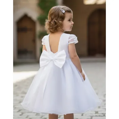 Menina de costas com vestido branco de saia de tule, decote nas costas, laço grande e mangas curtas transparentes