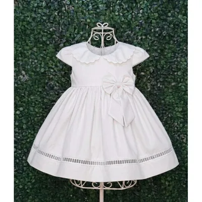 Vestido infantil branco com gola boneca ondulada, laço na cintura e faixa vazada na barra, em suporte de arame