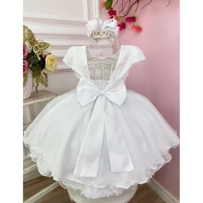 Vestido infantil branco visto de costas em cabide, com decote aberto, laço grande e saia de tule com brilho