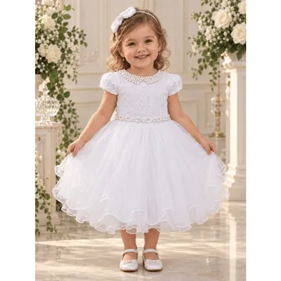 Menina com vestido branco de gola de pérolas, mangas bufantes, cinto perolado e saia de tule ondulada, em salão com rosas