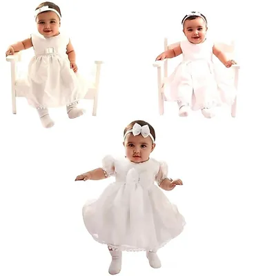 Três bebês com vestidos de batizado claros, tiara na cabeça e meias brancas, dois sentados em banquinhos brancos