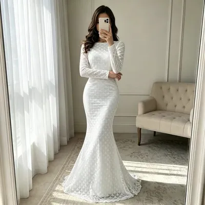 Mulher de vestido branco longo sereia, manga comprida e textura de escamas, fazendo foto no espelho de uma sala clara