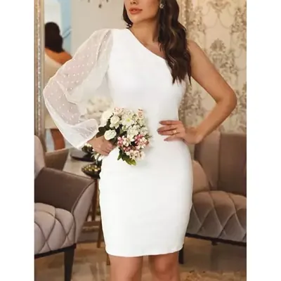 Mulher com vestido branco curto e justo de um ombro só, manga longa de tule poá e buquê de flores claras na mão