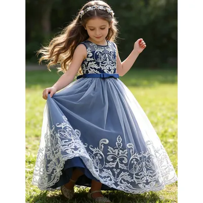 Menina girando num gramado com vestido longo azul-marinho sem mangas, renda prateada no corpo e na barra, faixa com laço