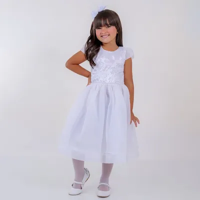 Menina sorrindo com vestido branco de corpo bordado, cinto de pérolas, mangas curtas e saia rodada transparente