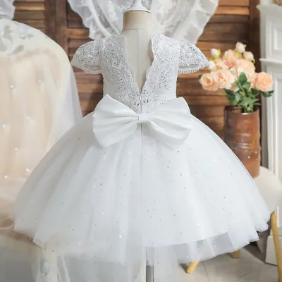 Vestido infantil branco visto de costas, com renda bordada, decote em V, laço grande de cetim e saia de tule com brilhos