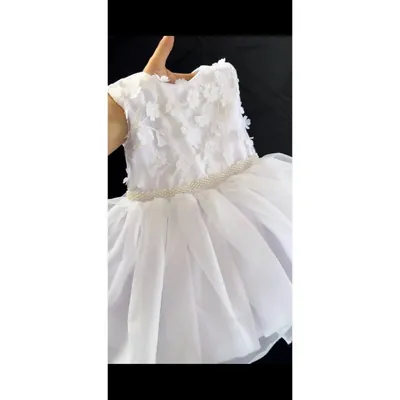 Vestido infantil branco seguro pela mão, com flores aplicadas em relevo no corpo, cinto de pérolas e saia em camadas