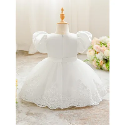Vestido infantil branco visto de costas em manequim, mangas bufantes, zíper, faixa na cintura e saia de tule com renda