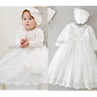 Bebê sentada com vestido longo branco de renda, manga longa e touca; ao lado, o mesmo vestido e a touca no cabide