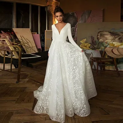 Noiva em vestido branco de manga longa, decote V e saia de renda com cauda, num ateliê com telas de pintura