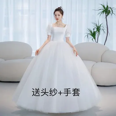 Noiva com vestido branco de decote quadrado, mangas bufantes curtas e saia rodada longa, em sala com sofás brancos