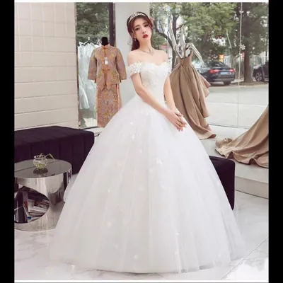 Noiva com vestido branco ombro a ombro, corpete rendado e saia de tule armada com florzinhas aplicadas, em loja de noivas