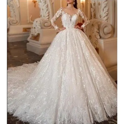 Noiva em salão clássico com vestido princesa de renda, mangas longas transparentes, saia volumosa e cauda longa
