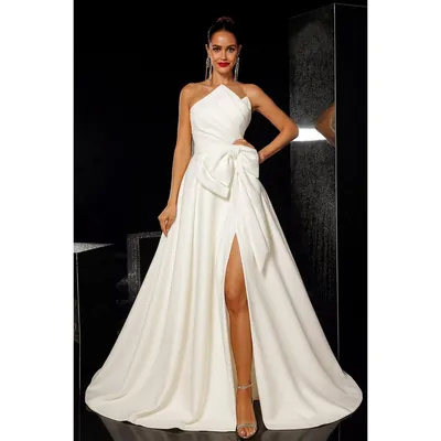 Noiva em fundo escuro com vestido branco tomara que caia, decote em dobras, laço grande na cintura, fenda e cauda