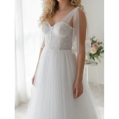 Noiva com vestido de corpete bordado em decote coração, alças de tule caídas nos braços e saia fluida de tule