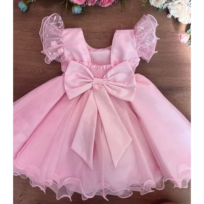 Vestido rosa de bebê visto de costas, com laço grande, mangas de tule bordado e barra ondulada