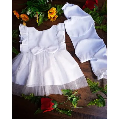 Vestido infantil branco com saia de tule brilhoso, laço na cintura e bolero branco de manga longa sobre mesa de madeira
