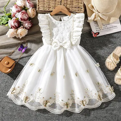Vestido infantil marfim em cabide, com babados nos ombros, laço e saia de tule com borboletas bordadas