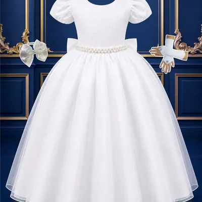 Vestido infantil branco longo com manga bufante, cinto de pérolas, laço na cintura e saia de tule, ao lado de luvas e laço