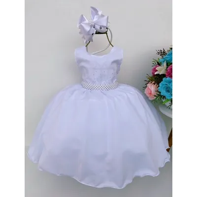 Vestido infantil branco sem mangas com strass no corpo, faixa de pérolas e saia armada, ao lado de laço de cabelo