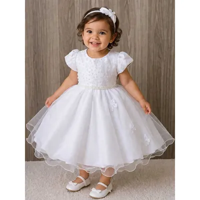 Menina pequena sorrindo com vestido branco de saia de tule, borboletas aplicadas, cinto de pérolas e mangas bufantes